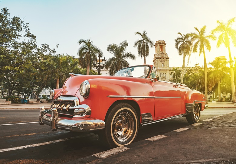 Classic American car against the background of palm trees in bright sun in the evening in Havana against the background of colonial architecture